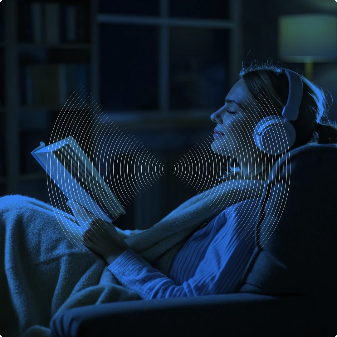 A woman wearing headphones, reading a book in a dark room with a blue glow.