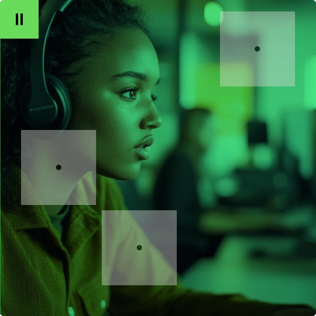 A young woman wearing headphones, focused on a computer screen in a green-lit room.
