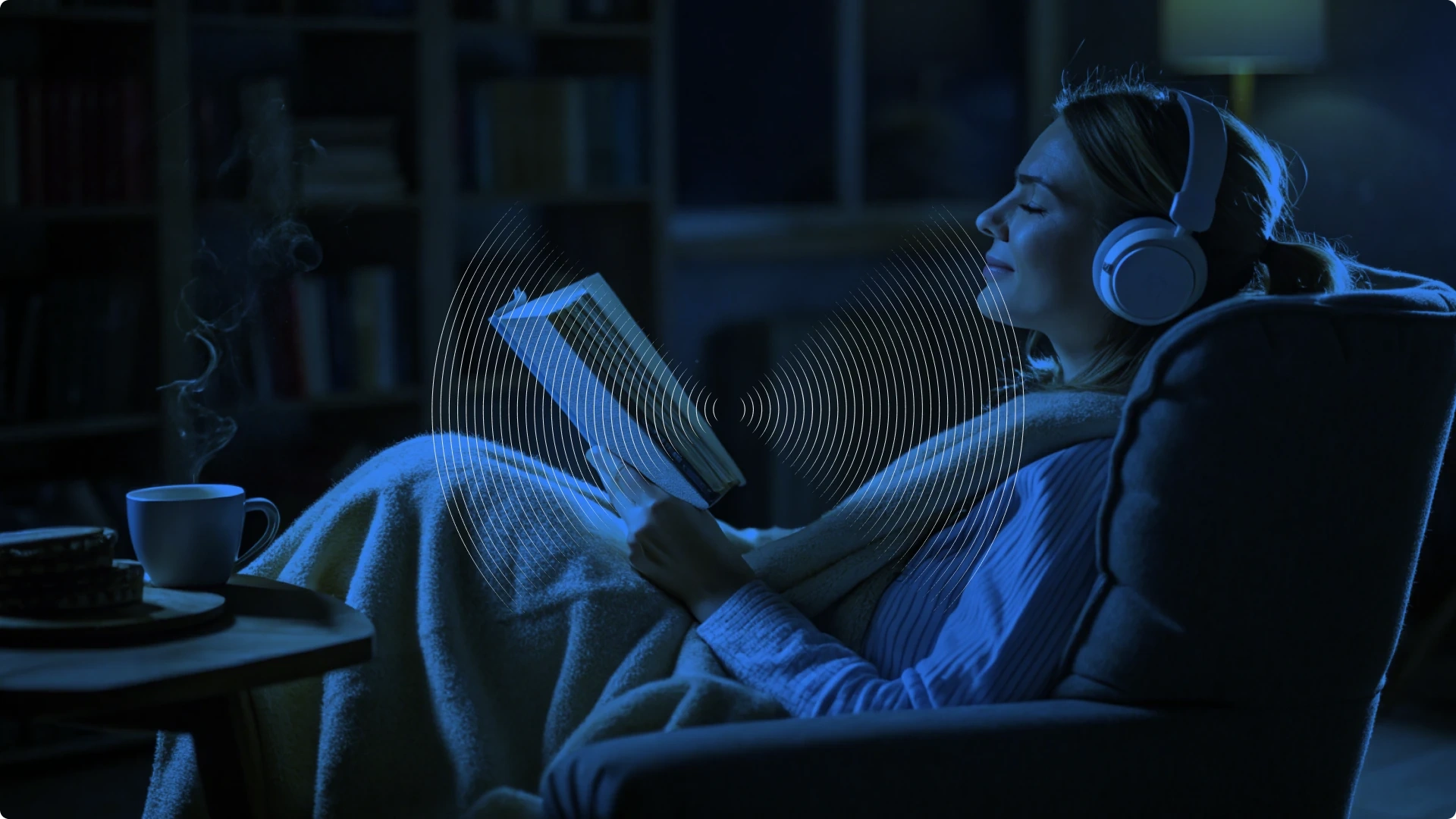 A woman relaxing in a chair, listening to music with headphones, reading a book, and enjoying a hot beverage in a cozy, dimly lit room.