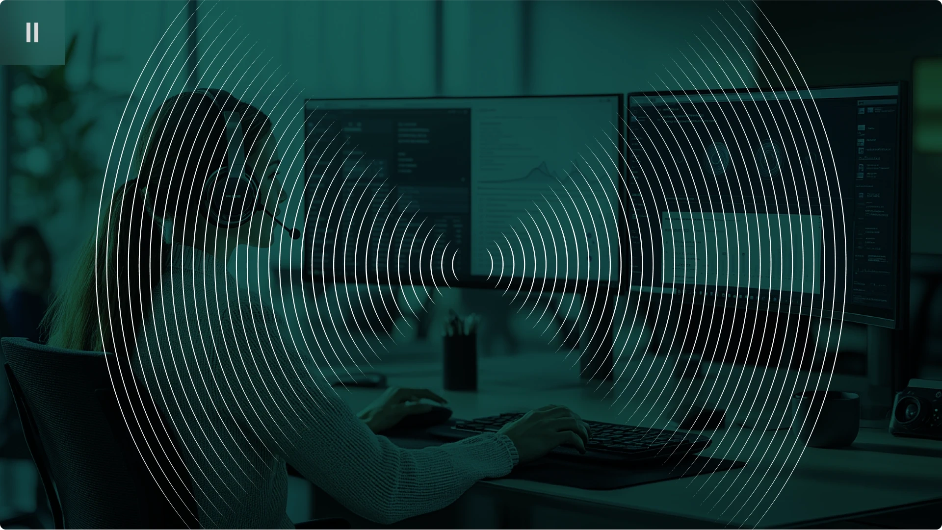 Person working at a computer with dual monitors, wearing a headset.