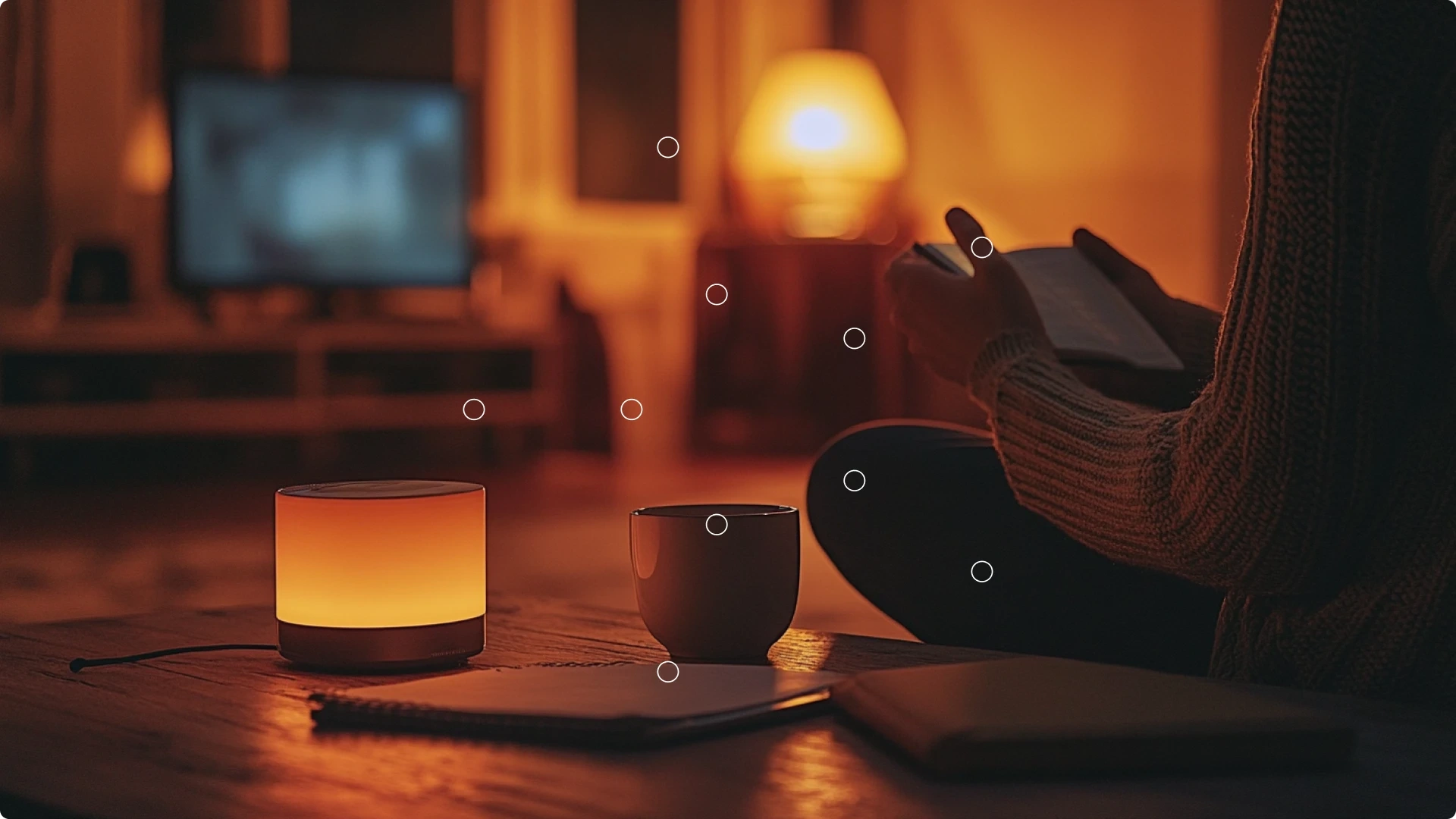 A person sitting on the floor reading a book, with a lit candle and a mug on a wooden table in a cozy, dimly lit room.